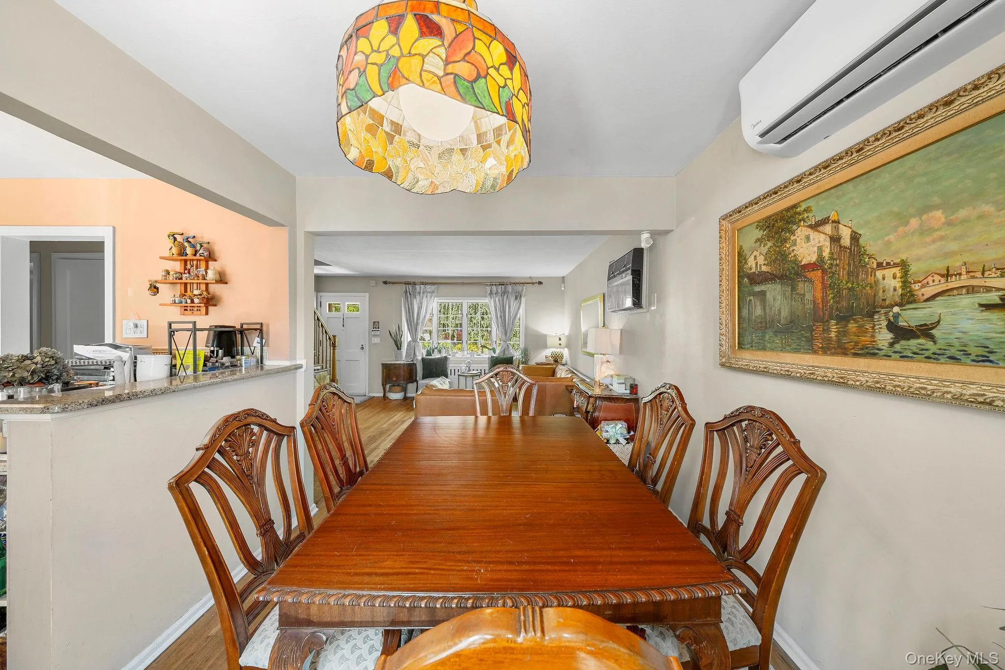 Dining area featuring a decorative stained-glass ceiling fixture, wood-finish flooring, and a granite-top half wall that leads into the kitchen. Dining area featuring a decorative stained-glass ceiling fixture, wood-finish flooring, and a granite-top half wall that leads into the kitchen.