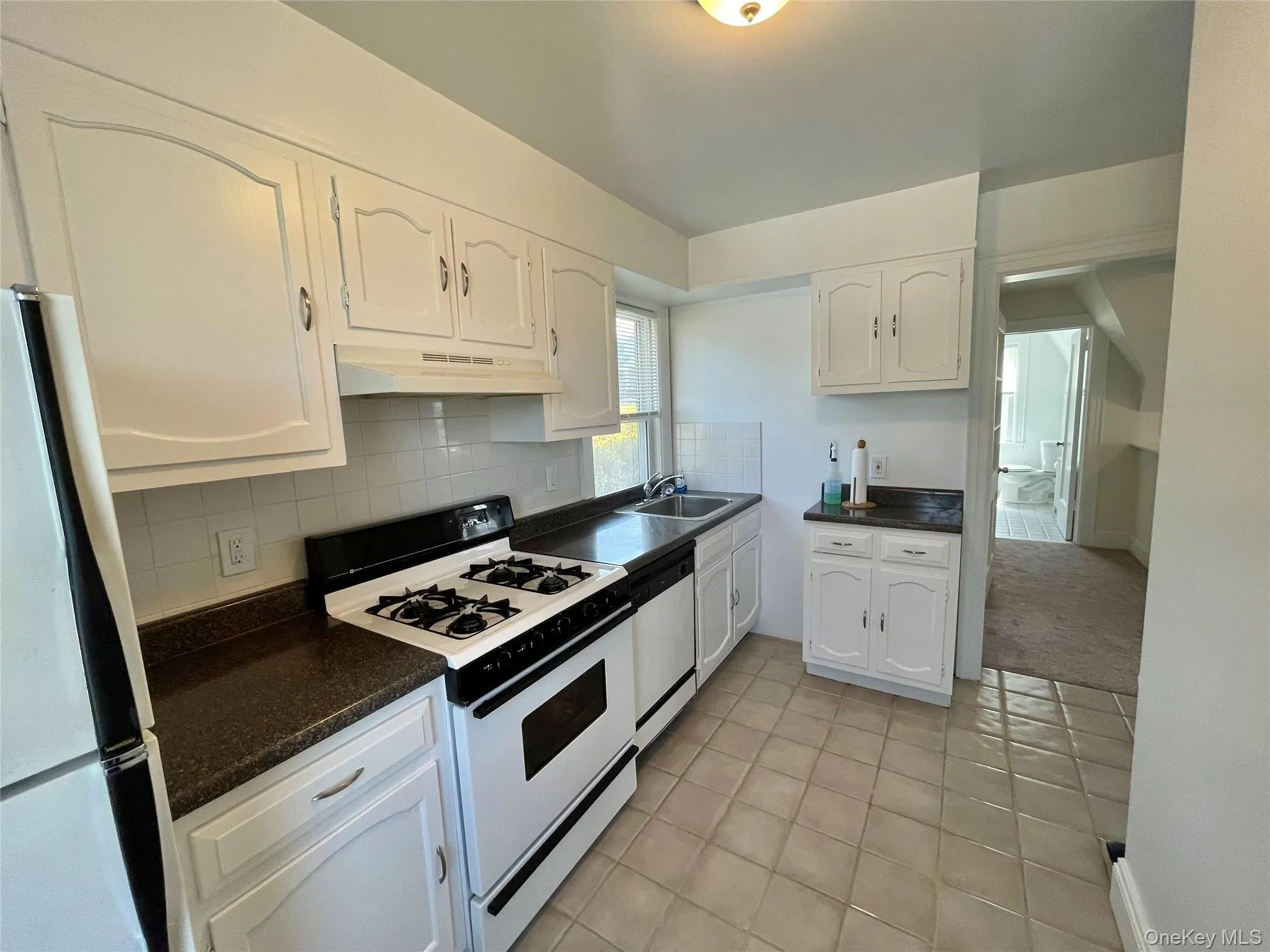 Kitchen with a sink, white cabinetry, white appliances, under cabinet range hood, and light tile patterned floors Kitchen with a sink, white cabinetry, white appliances, under cabinet range hood, and light tile patterned floors