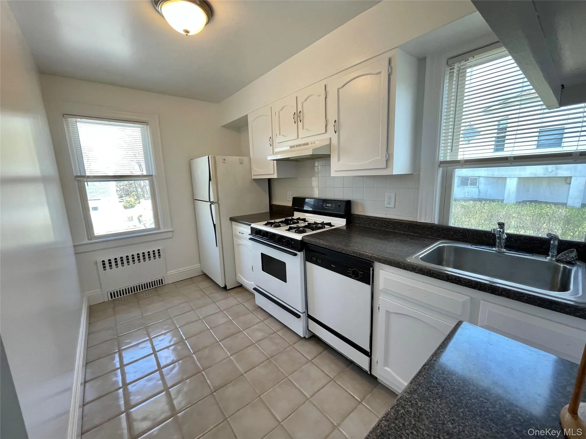 Kitchen with radiator heating unit, under cabinet range hood, dark countertops, a sink, and white appliances Kitchen with radiator heating unit, under cabinet range hood, dark countertops, a sink, and white appliances