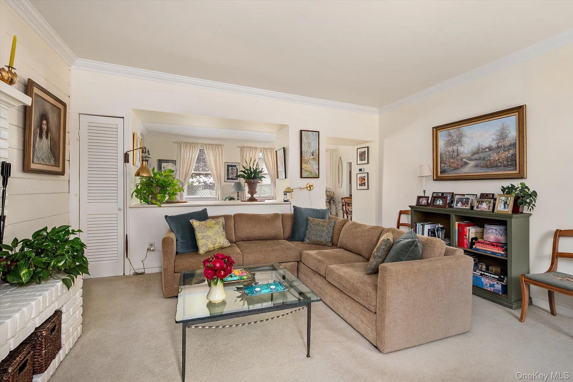 Carpeted living area featuring a white brick fireplace, crown molding, and a partial wall separating spaces Carpeted living area featuring a white brick fireplace, crown molding, and a partial wall separating spaces