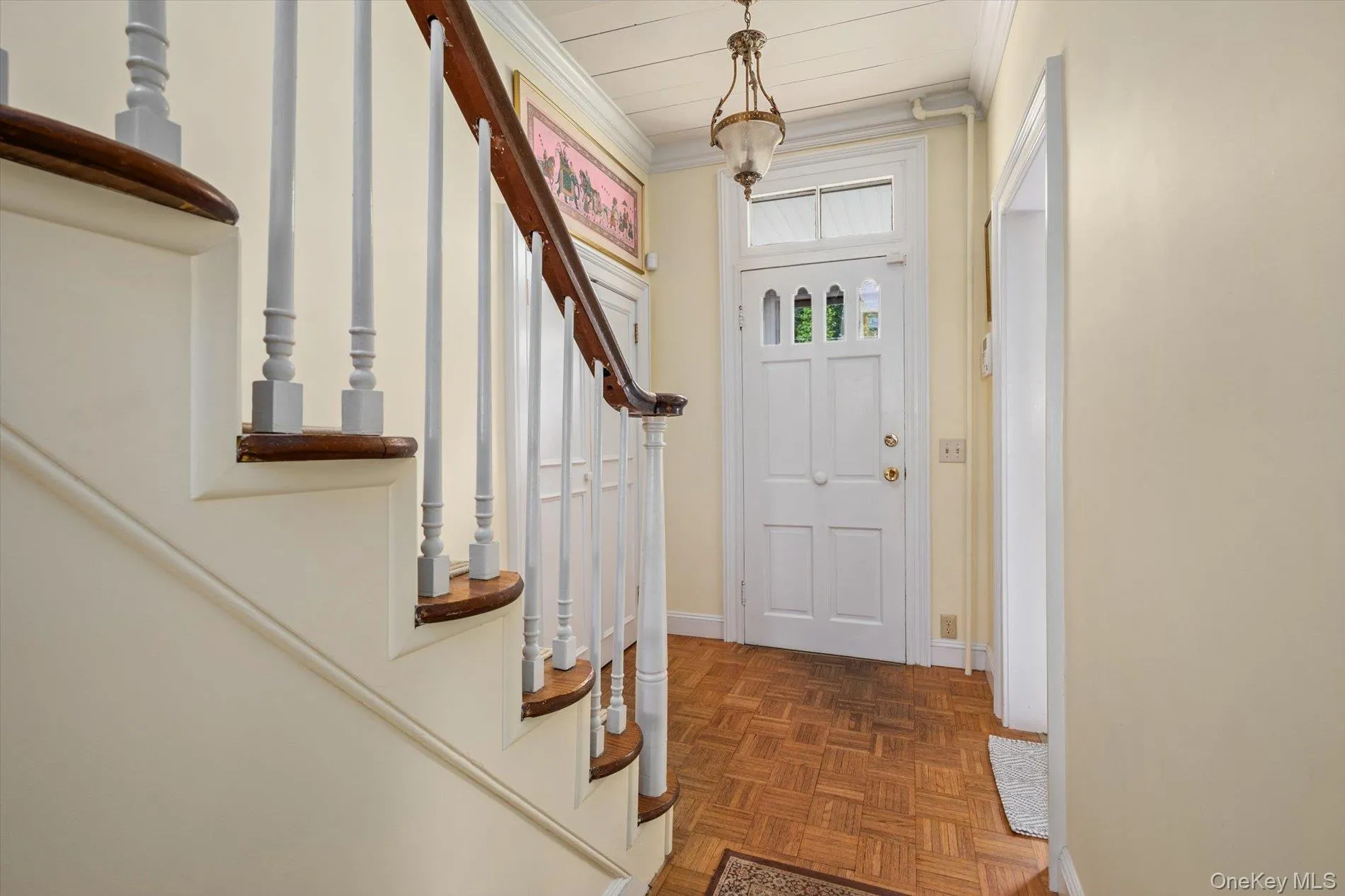 Inviting entryway featuring wood-finish parquet flooring, a classic white paneled door with glass inserts, and a bronze pendant light fixture Inviting entryway featuring wood-finish parquet flooring, a classic white paneled door with glass inserts, and a bronze pendant light fixture
