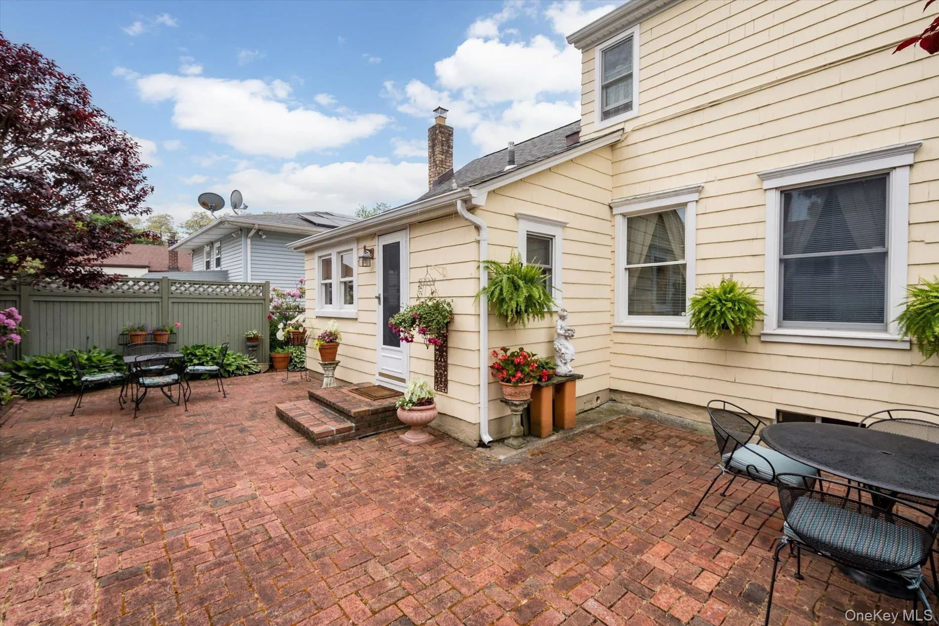 Expansive brick patio featuring a lattice-topped fence, mature red-leaf tree, and exterior access to the residence Expansive brick patio featuring a lattice-topped fence, mature red-leaf tree, and exterior access to the residence