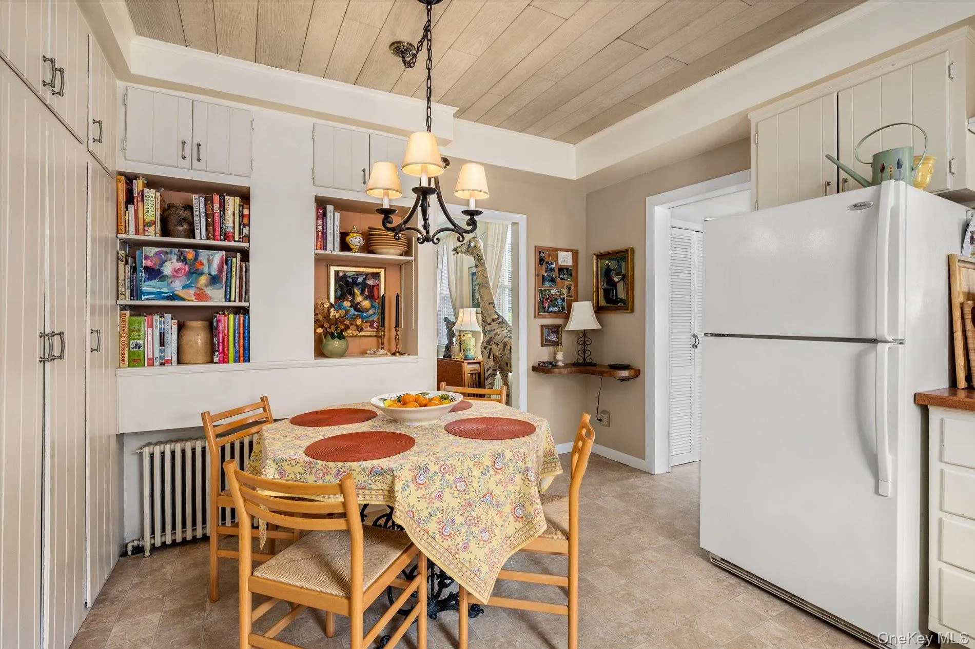 Integrated kitchen and dining area featuring a wood-panel ceiling, built-in shelving, white cabinetry, and a black iron chandelier Integrated kitchen and dining area featuring a wood-panel ceiling, built-in shelving, white cabinetry, and a black iron chandelier