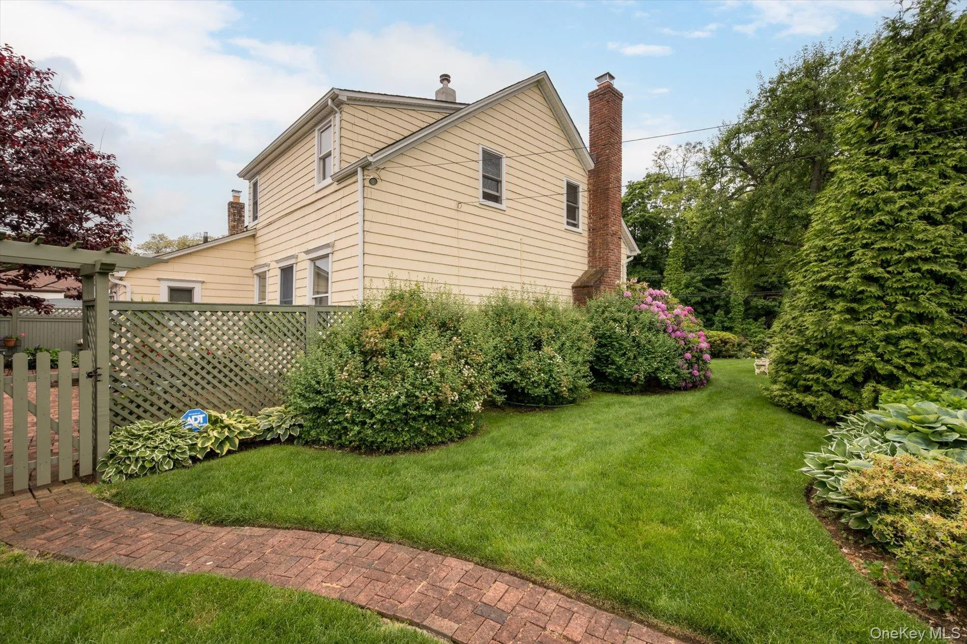 Expansive backyard featuring a manicured lawn, a winding brick paver pathway, and mature landscaping with various shrubs and flowering plants Expansive backyard featuring a manicured lawn, a winding brick paver pathway, and mature landscaping with various shrubs and flowering plants