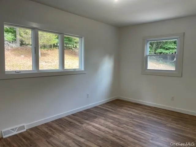 Unfurnished room featuring dark wood-type flooring and plenty of natural light Unfurnished room featuring dark wood-type flooring and plenty of natural light