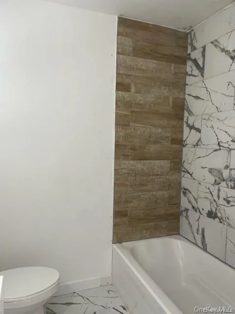Bathroom featuring tile floors, tiled shower / bath, and toilet Bathroom featuring tile floors, tiled shower / bath, and toilet