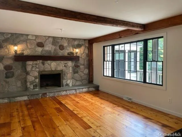 Unfurnished living room featuring plenty of natural light, beam ceiling, a fireplace, and wood-type flooring Unfurnished living room featuring plenty of natural light, beam ceiling, a fireplace, and wood-type flooring