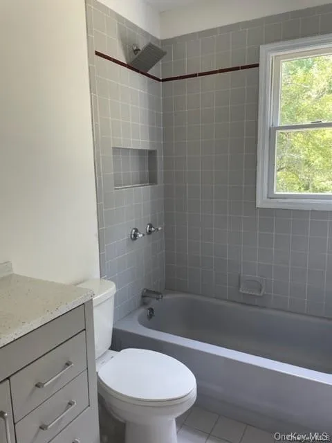 Full bathroom featuring a wealth of natural light, tiled shower / bath combo, vanity, and toilet Full bathroom featuring a wealth of natural light, tiled shower / bath combo, vanity, and toilet