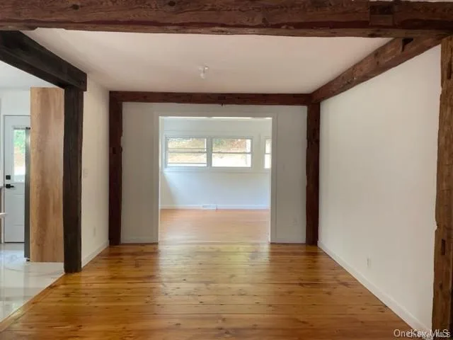 Empty room featuring beamed ceiling, a healthy amount of sunlight, and light hardwood / wood-style flooring Empty room featuring beamed ceiling, a healthy amount of sunlight, and light hardwood / wood-style flooring