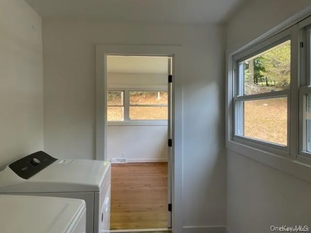 Laundry area featuring a healthy amount of sunlight, washer and clothes dryer, and hardwood / wood-style floors Laundry area featuring a healthy amount of sunlight, washer and clothes dryer, and hardwood / wood-style floors
