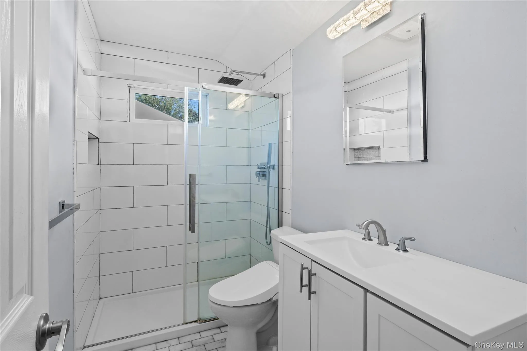 Modern bathroom featuring a glass-enclosed shower with white subway tile, a built-in shower niche, and a transom window Modern bathroom featuring a glass-enclosed shower with white subway tile, a built-in shower niche, and a transom window