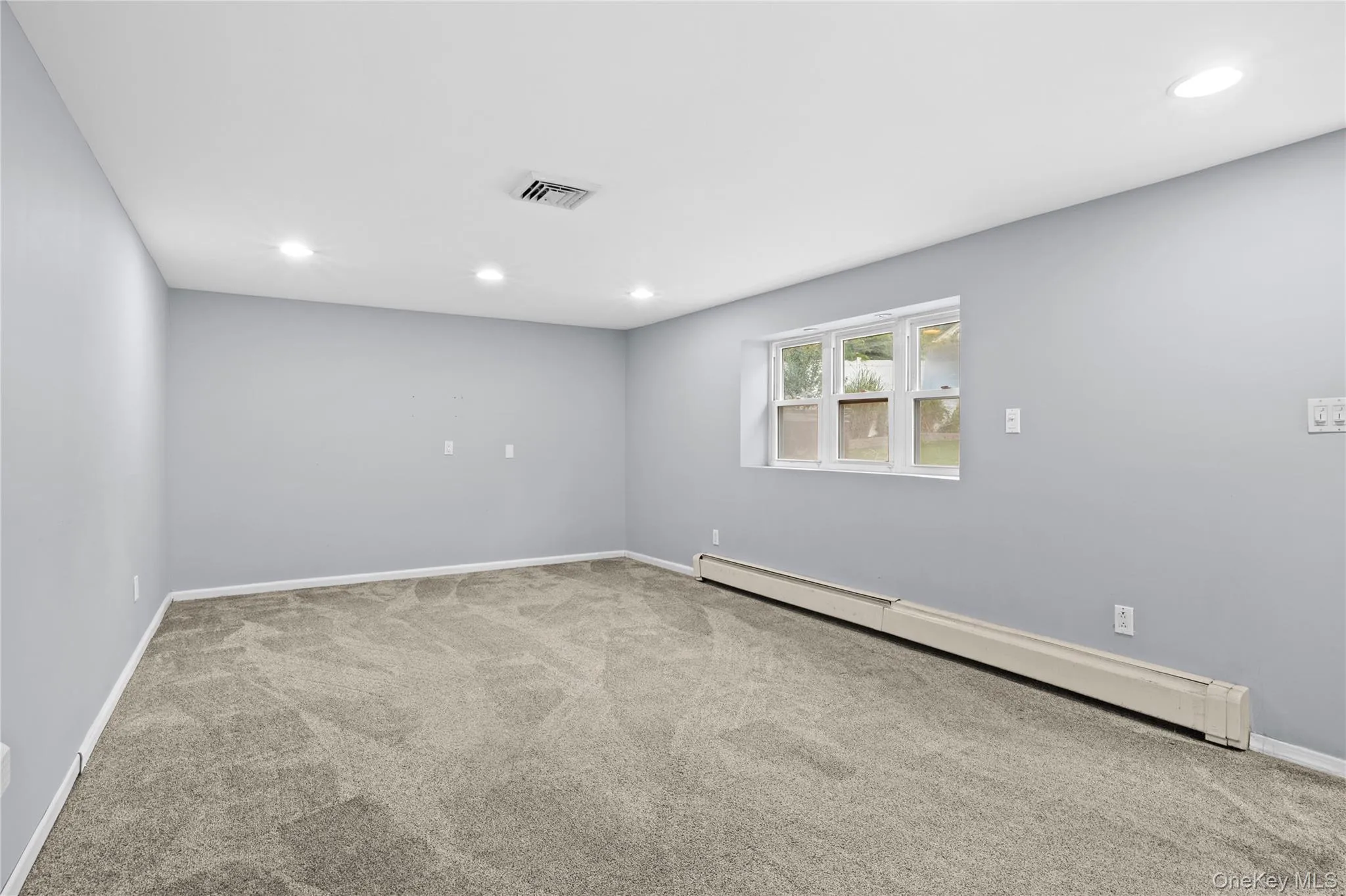 Spacious interior room featuring light grey wall paint, plush grey carpeting, and recessed ceiling lighting Spacious interior room featuring light grey wall paint, plush grey carpeting, and recessed ceiling lighting