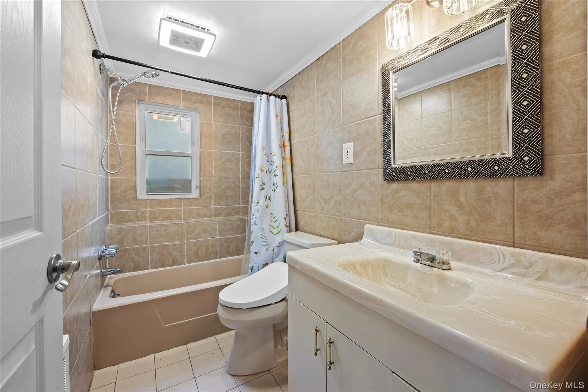 Bathroom featuring a tiled shower surround, a single window, a vanity with an integrated sink, a wall-mounted mirror, and overhead lighting Bathroom featuring a tiled shower surround, a single window, a vanity with an integrated sink, a wall-mounted mirror, and overhead lighting