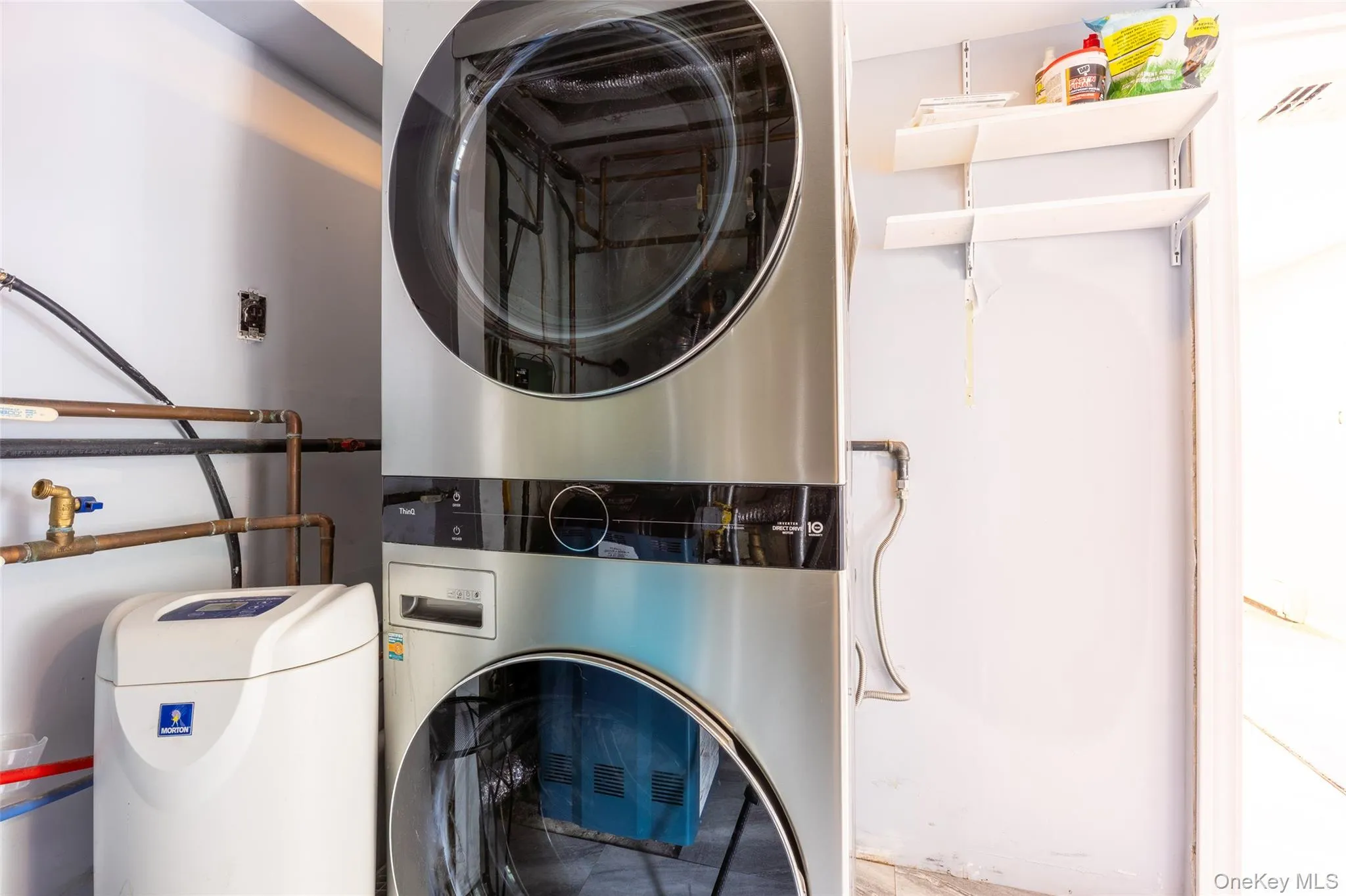Stacked stainless steel laundry appliances with a front-loading washer and dryer, accompanied by a white water softening system Stacked stainless steel laundry appliances with a front-loading washer and dryer, accompanied by a white water softening system