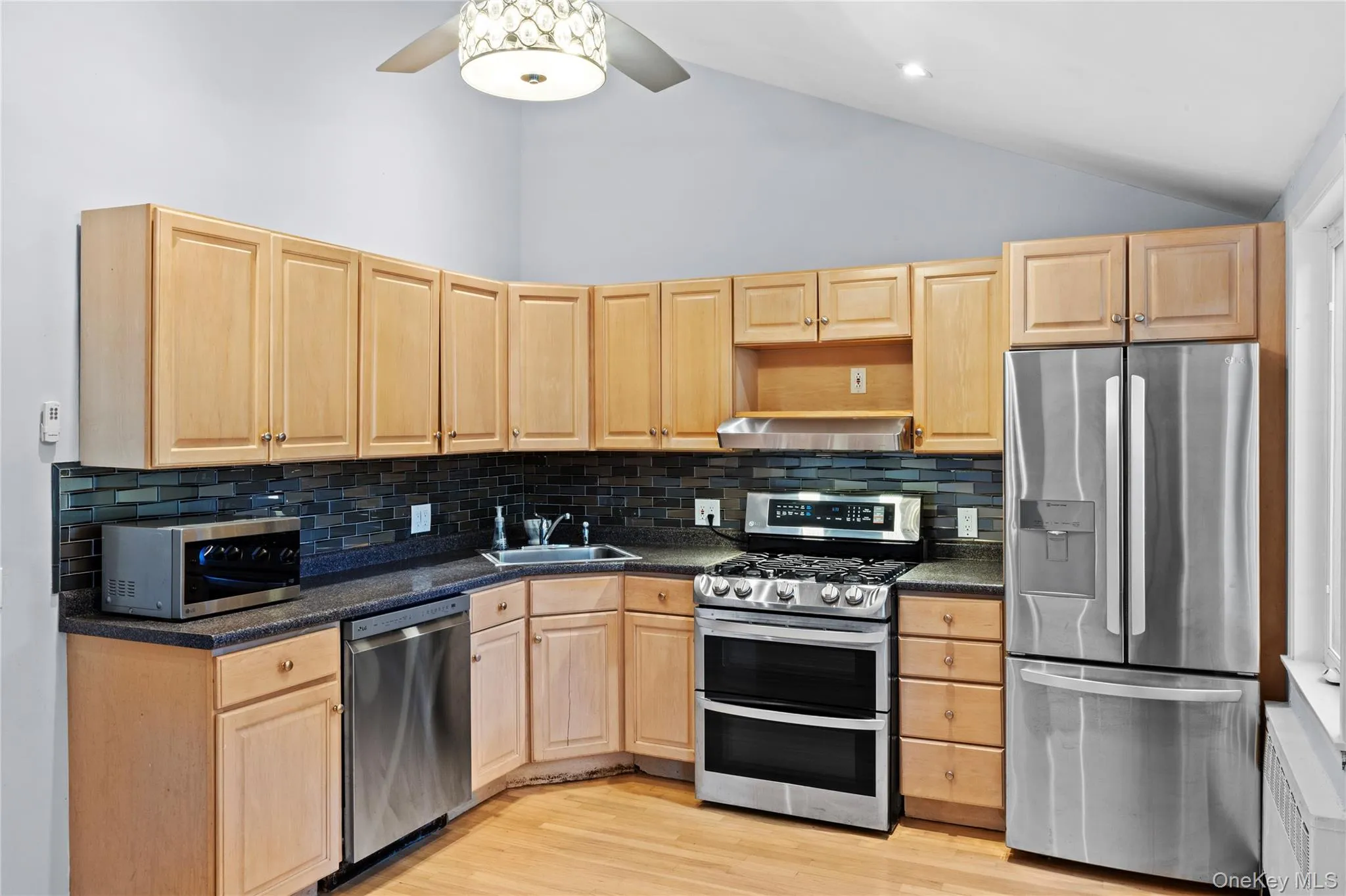 Kitchen featuring wood cabinetry, stone-finish countertops, black subway tile backsplash, and wood-finish flooring Kitchen featuring wood cabinetry, stone-finish countertops, black subway tile backsplash, and wood-finish flooring
