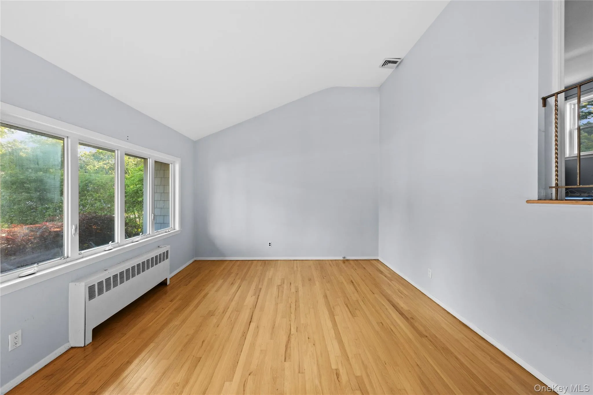 Room featuring multiple windows, sloped ceiling, wood-finish flooring, and light-toned walls Room featuring multiple windows, sloped ceiling, wood-finish flooring, and light-toned walls