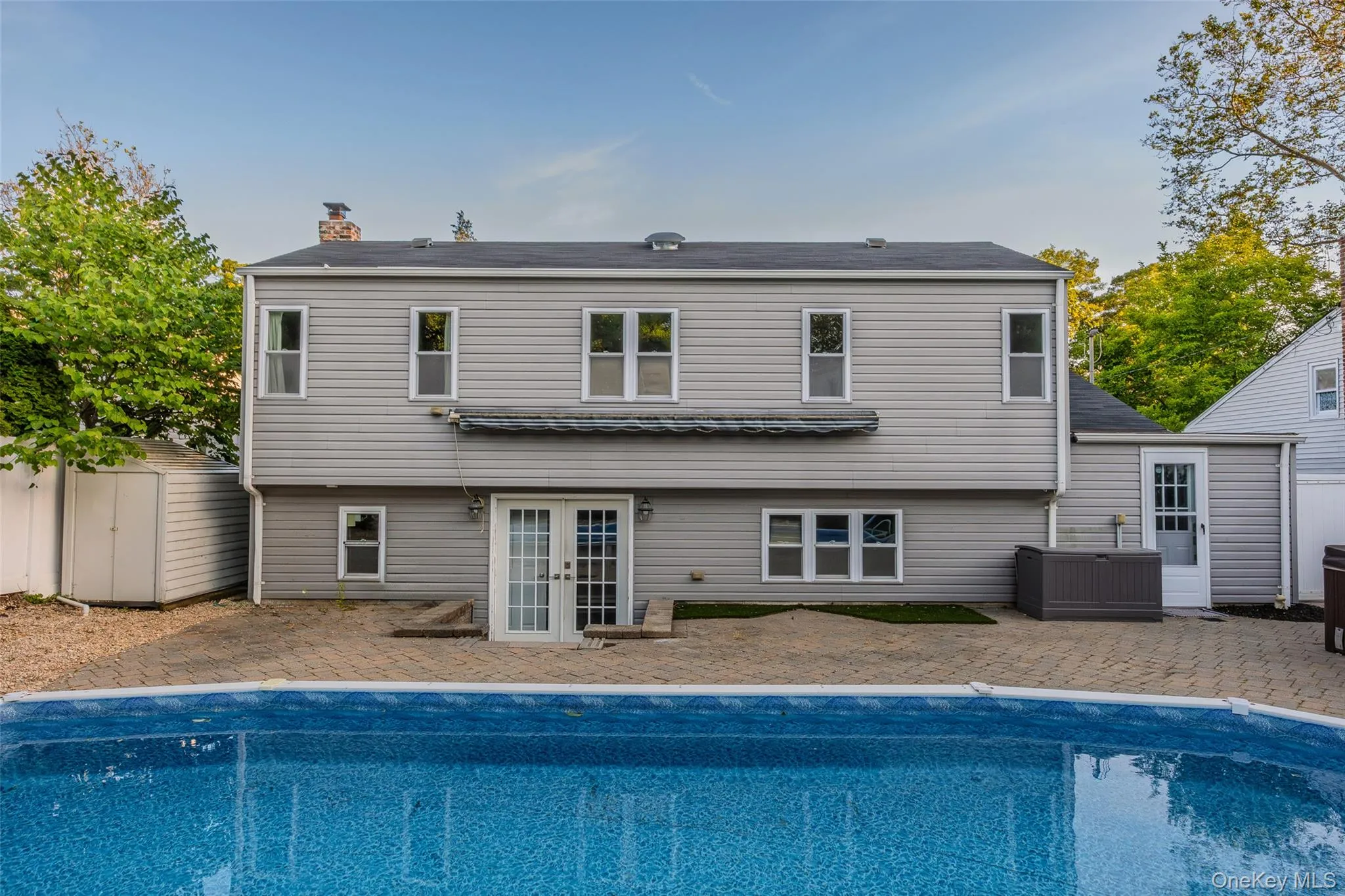 Rear exterior with an in-ground swimming pool, paver patio, light gray horizontal siding, and multiple windows Rear exterior with an in-ground swimming pool, paver patio, light gray horizontal siding, and multiple windows