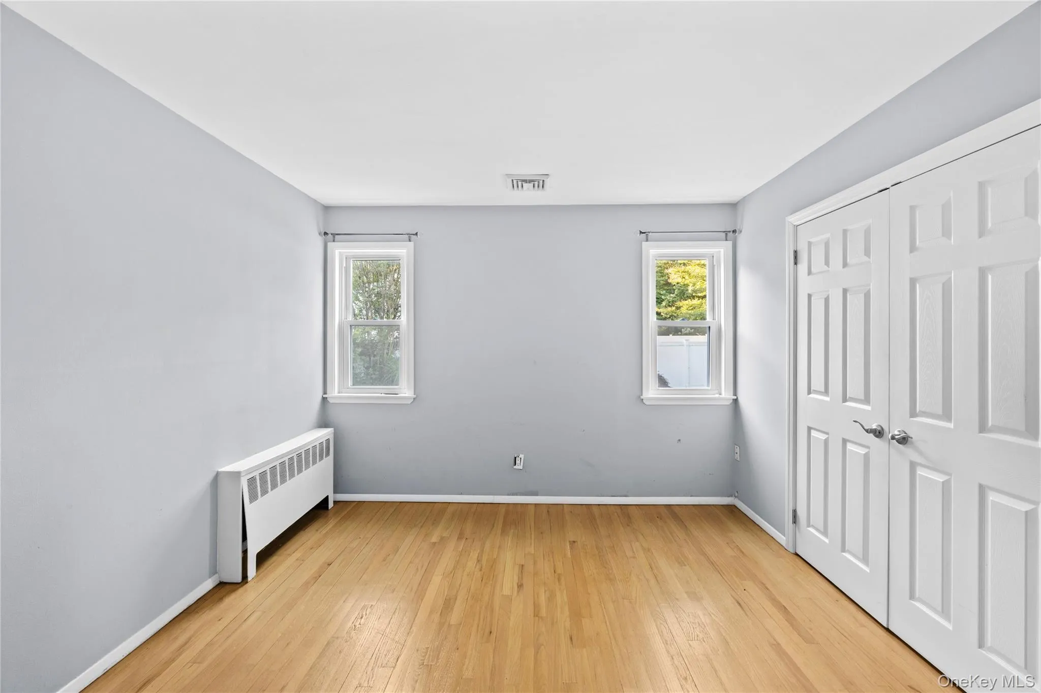 Hardwood flooring in a space featuring two double-pane windows with white trim Hardwood flooring in a space featuring two double-pane windows with white trim