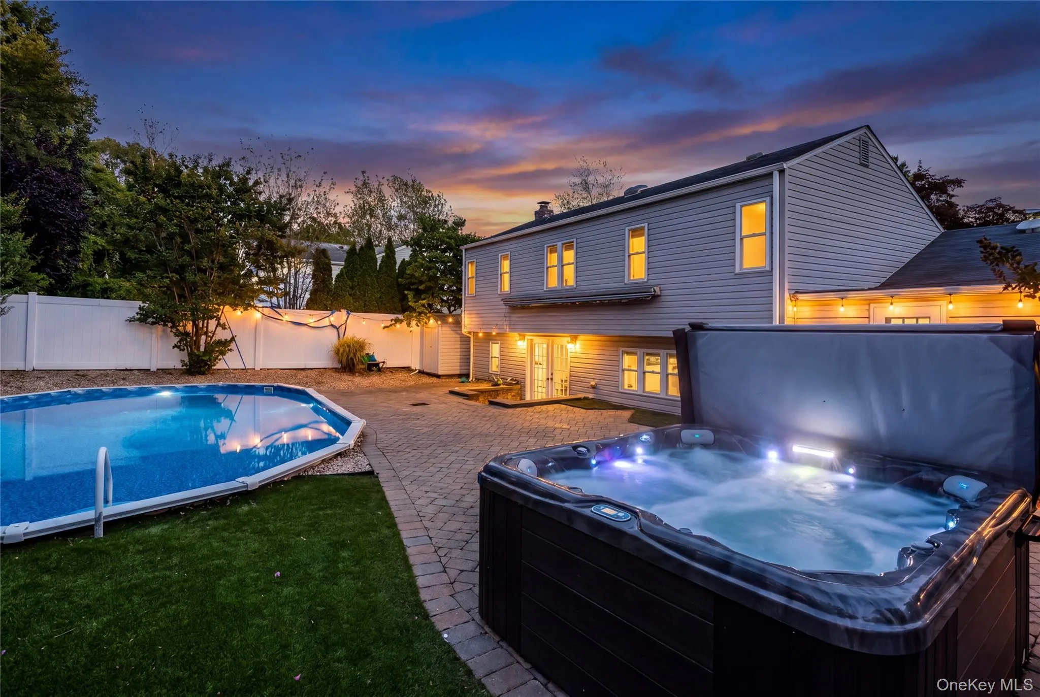Outdoor spa and swimming pool with integrated lighting, surrounded by a paver patio and a manicured lawn Outdoor spa and swimming pool with integrated lighting, surrounded by a paver patio and a manicured lawn