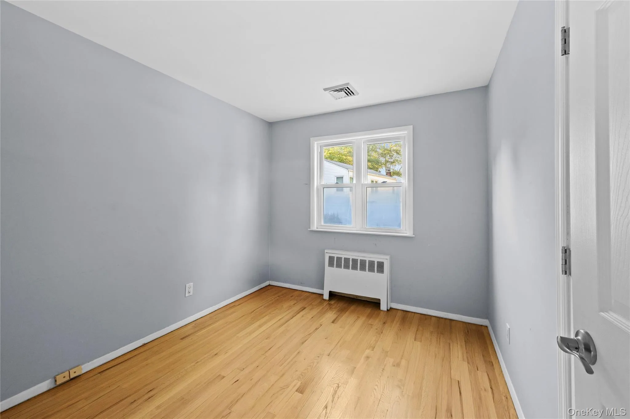Interior room featuring wood-finish flooring, light gray walls, white trim, and a double-hung window Interior room featuring wood-finish flooring, light gray walls, white trim, and a double-hung window
