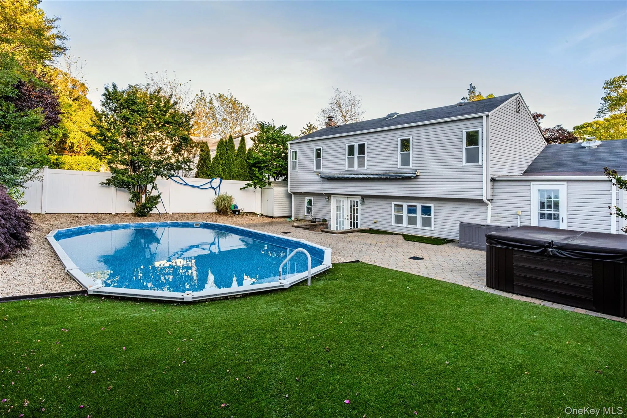 Expansive backyard featuring an above-ground swimming pool, artificial turf, and a paver patio Expansive backyard featuring an above-ground swimming pool, artificial turf, and a paver patio