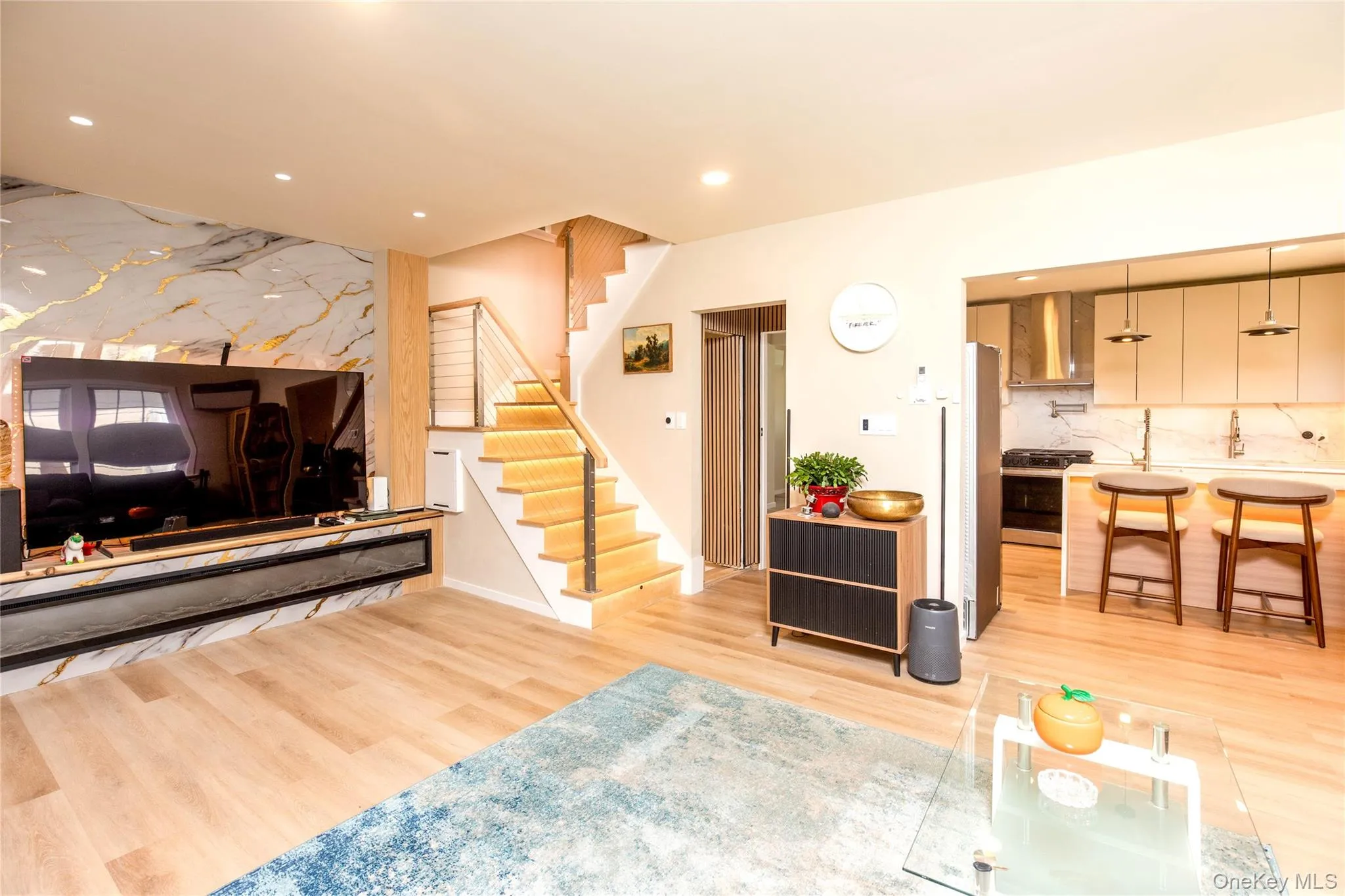 Open-concept living area featuring light wood-finish flooring, recessed lighting, and a modern staircase with cable railing Open-concept living area featuring light wood-finish flooring, recessed lighting, and a modern staircase with cable railing