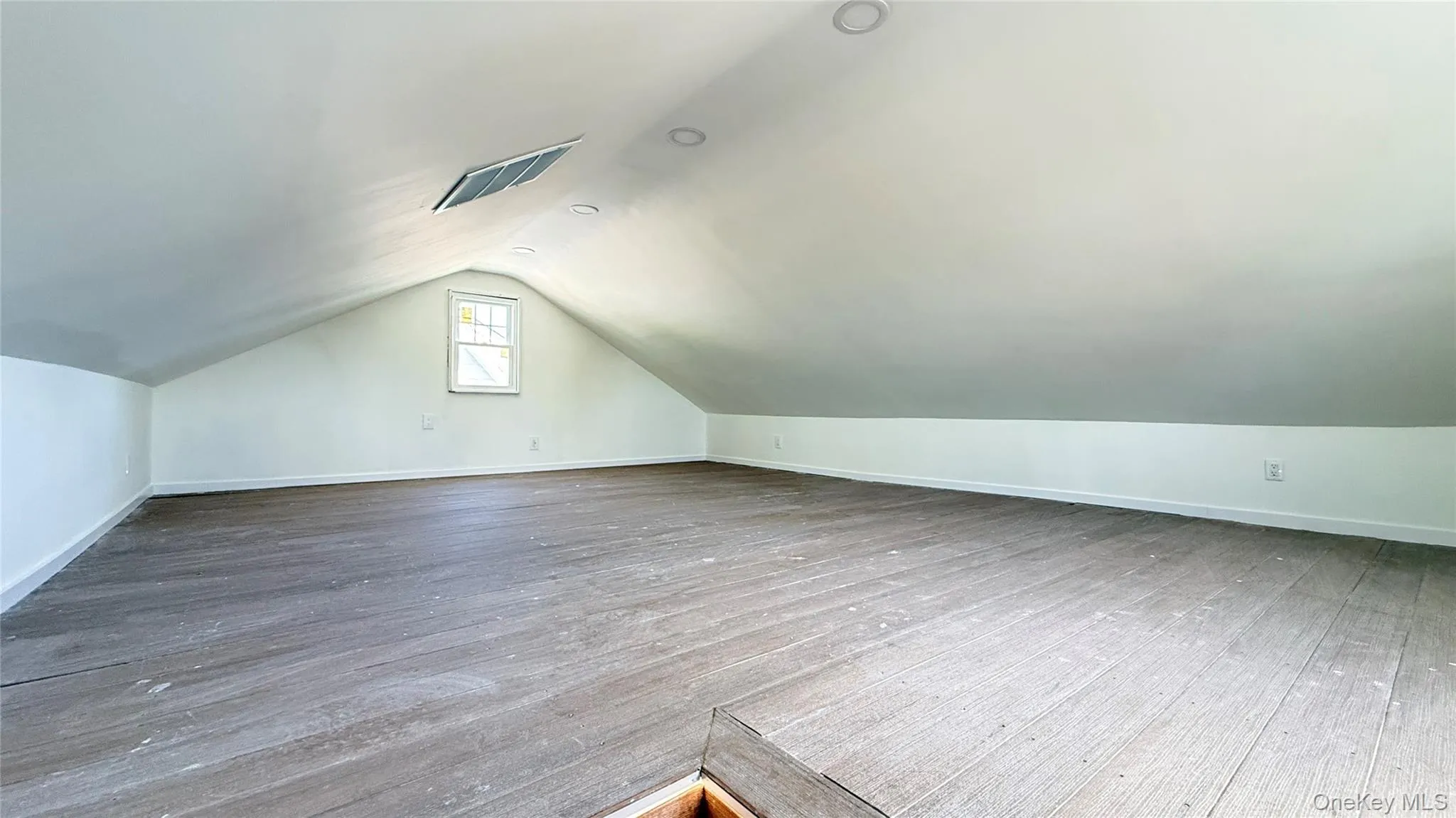 Expansive attic space featuring wood-finish flooring, a window, recessed lighting, and a sloped ceiling Expansive attic space featuring wood-finish flooring, a window, recessed lighting, and a sloped ceiling