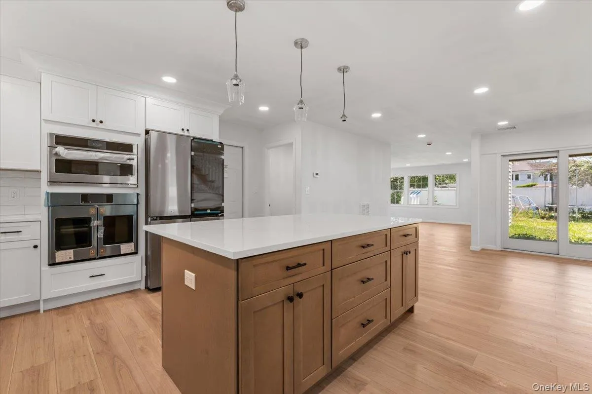 Contemporary kitchen featuring a large central island with a light-toned wood finish, white countertops, built-in stainless steel appliances, and white cabinetry Contemporary kitchen featuring a large central island with a light-toned wood finish, white countertops, built-in stainless steel appliances, and white cabinetry