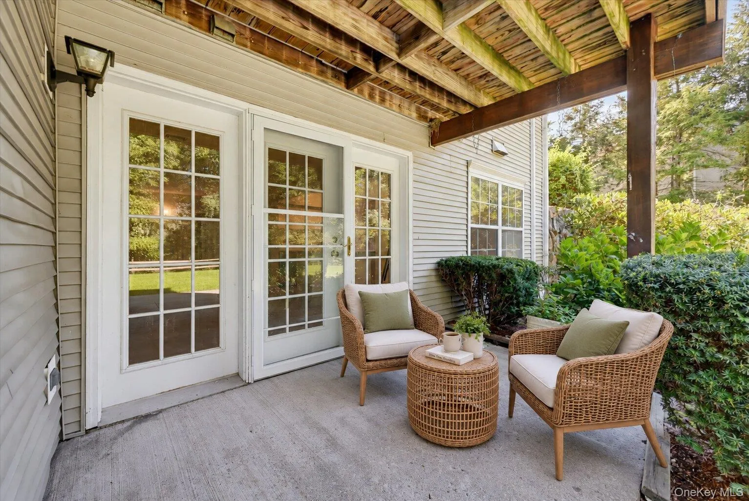 Virtually Staged. Alternate view of the covered patio showing French doors, outdoor seating, and surrounding landscaping. Virtually Staged. Alternate view of the covered patio showing French doors, outdoor seating, and surrounding landscaping.