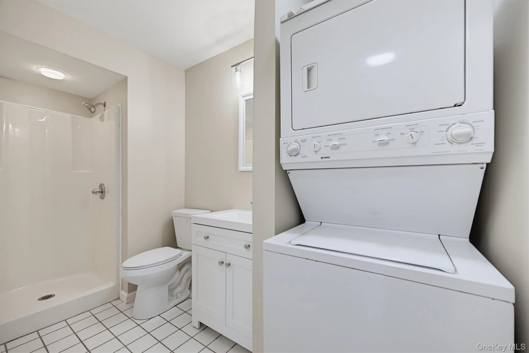 Full bathroom featuring a walk-in shower, white vanity, and convenient in-unit stacked washer and dryer. Full bathroom featuring a walk-in shower, white vanity, and convenient in-unit stacked washer and dryer.