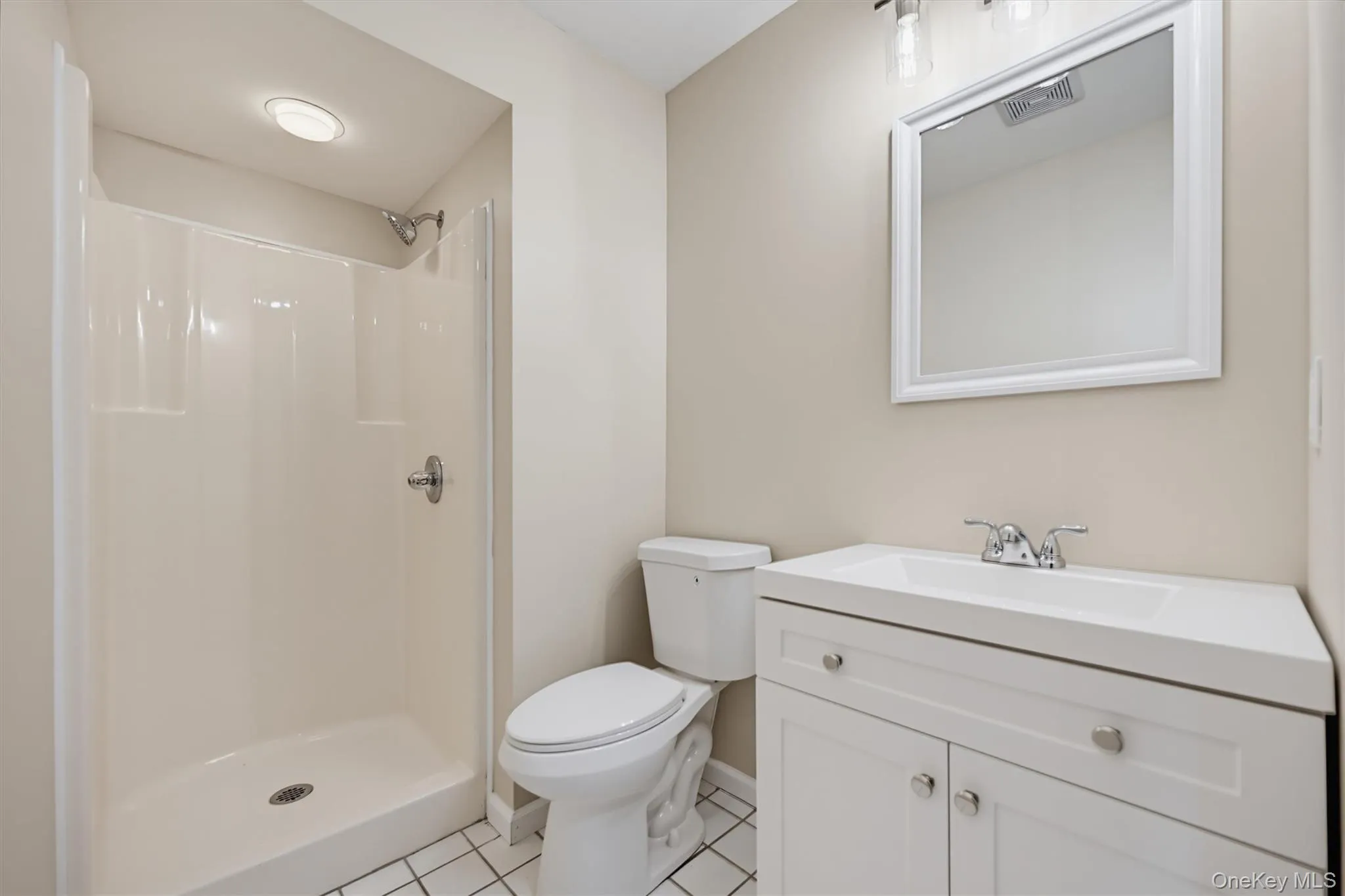 Full bathroom with walk-in shower, white vanity, and tiled flooring. Full bathroom with walk-in shower, white vanity, and tiled flooring.