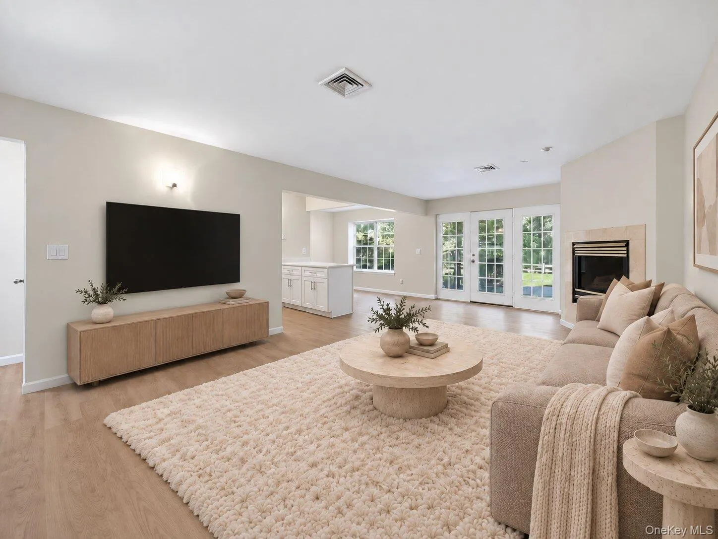 Virtually Staged. Spacious living area featuring light wood flooring, a cozy fireplace, abundant natural light, and French doors providing direct access to the outdoor space. Virtually Staged. Spacious living area featuring light wood flooring, a cozy fireplace, abundant natural light, and French doors providing direct access to the outdoor space.