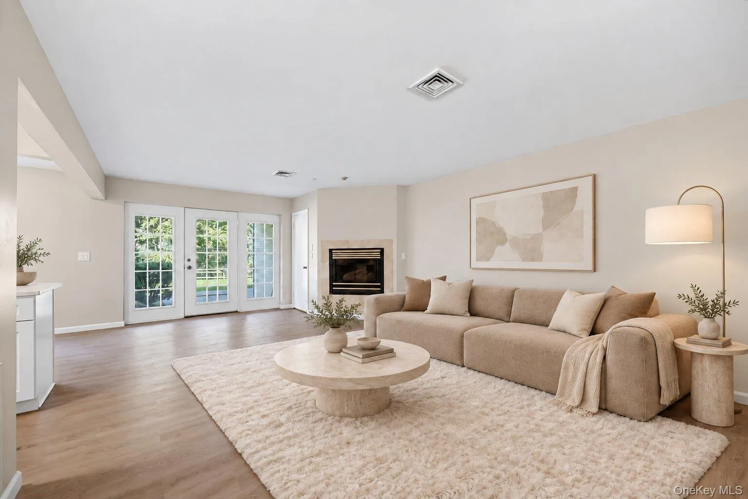 Virtually Staged. Open living room featuring a fireplace, light wood flooring, French doors, and an adjoining kitchen area. Virtually Staged. Open living room featuring a fireplace, light wood flooring, French doors, and an adjoining kitchen area.