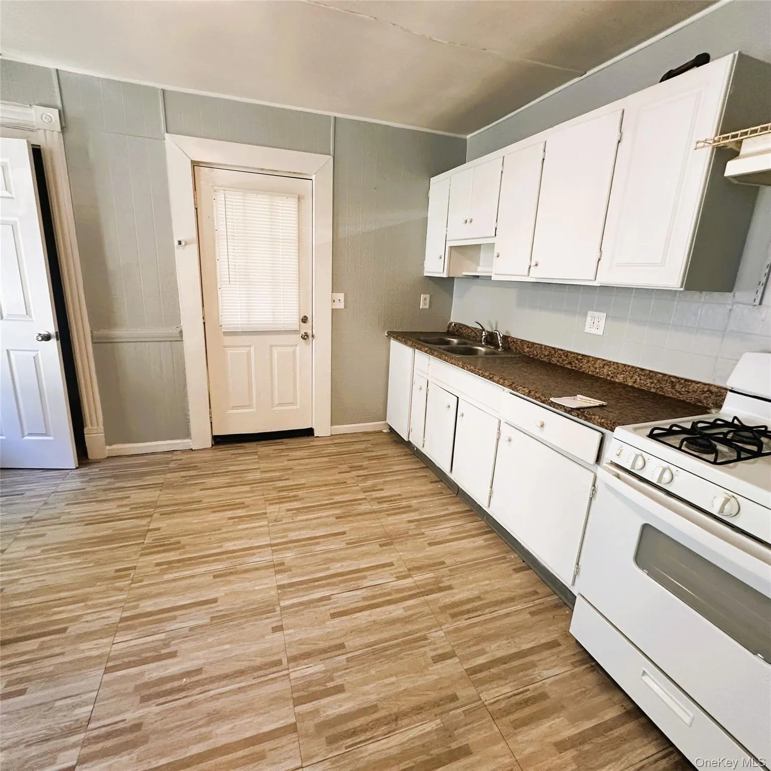 Vinyl flooring, white cabinetry, gas stove, hood, rear entrance. Vinyl flooring, white cabinetry, gas stove, hood, rear entrance.