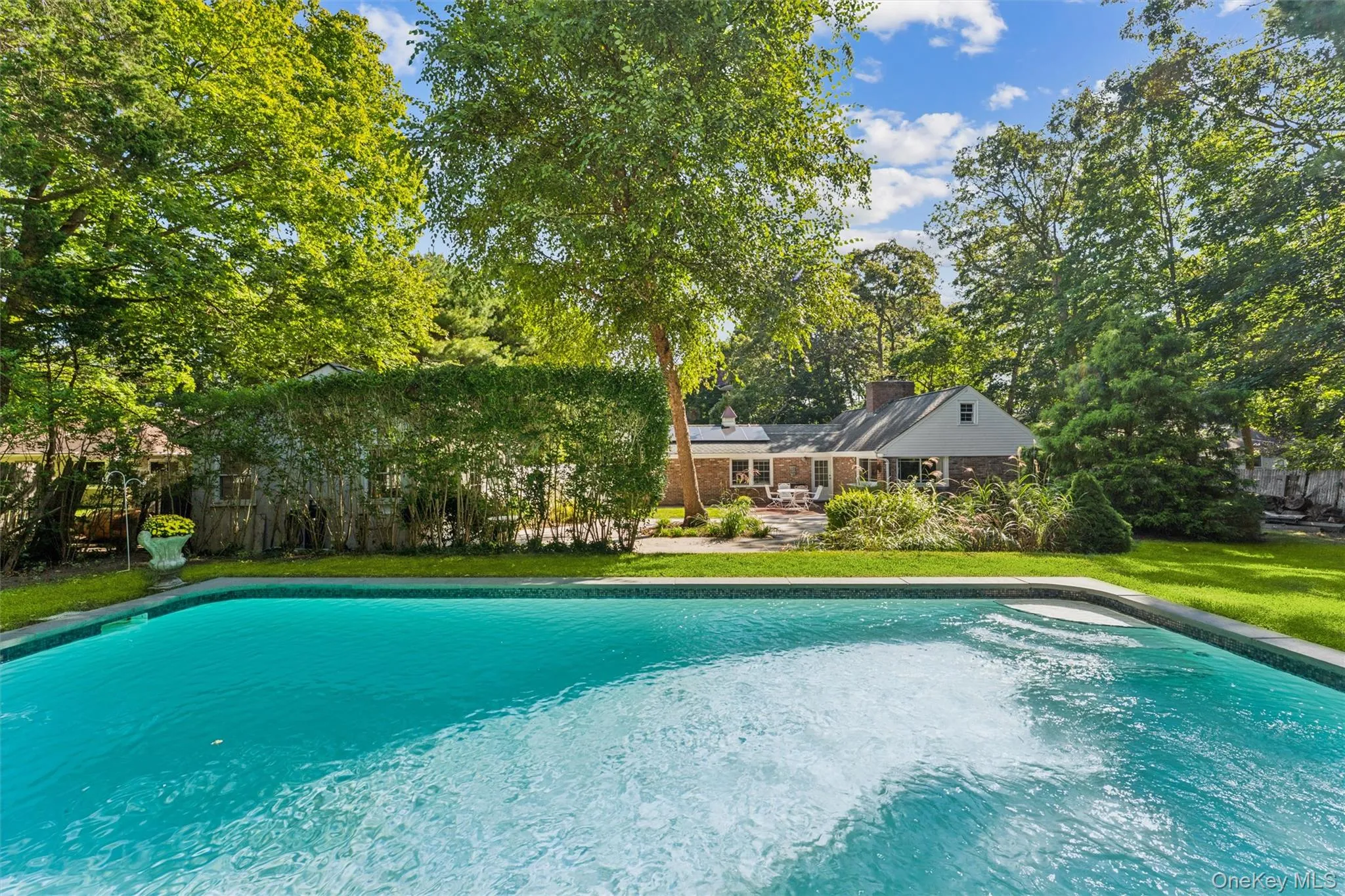 In-ground swimming pool with integrated steps, surrounded by a stone coping, expansive green lawn, and mature trees In-ground swimming pool with integrated steps, surrounded by a stone coping, expansive green lawn, and mature trees
