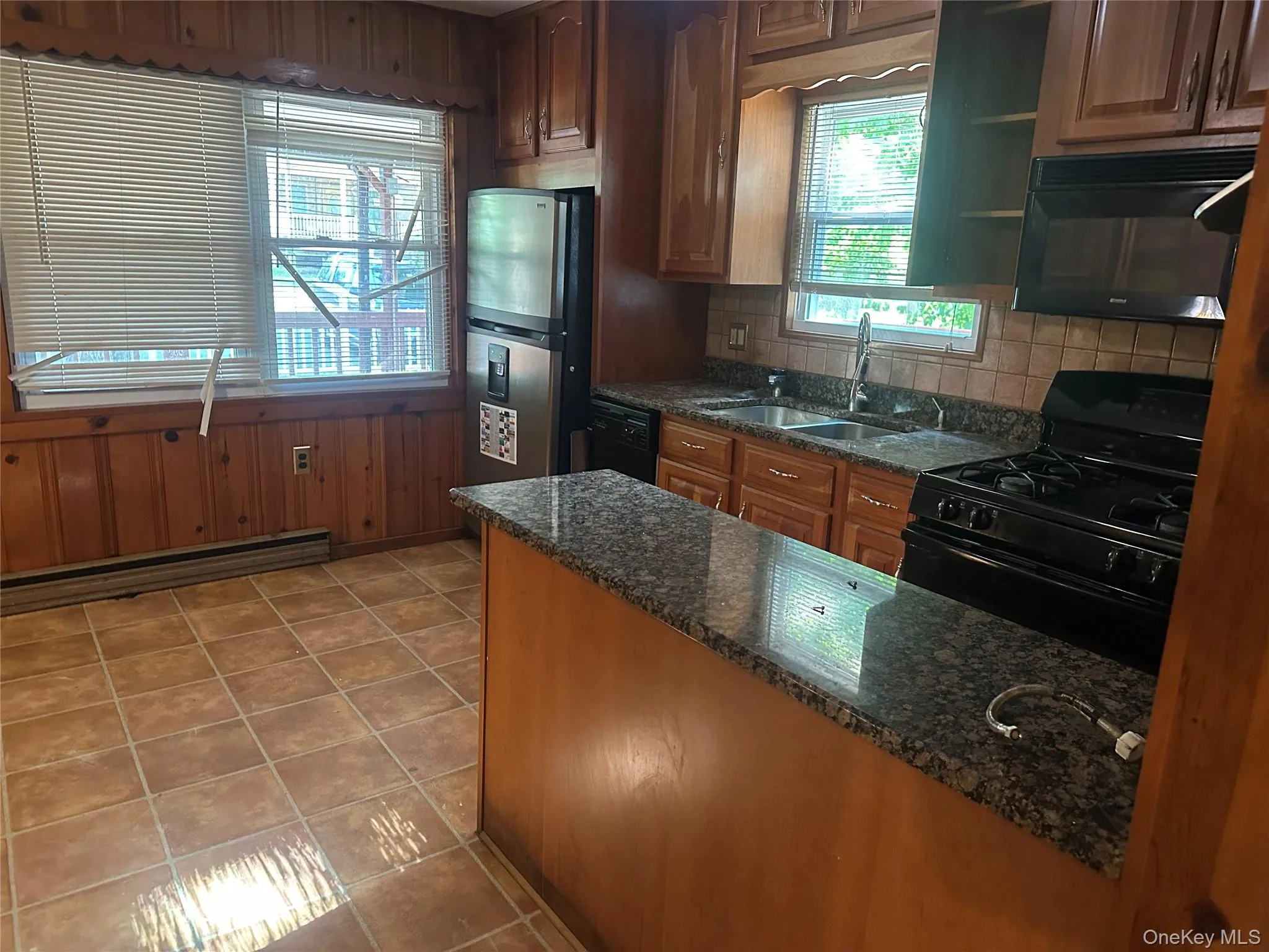 Kitchen featuring wood paneling, tile flooring, granite-style countertops, stainless steel refrigerator, and a gas range with an overhead microwave Kitchen featuring wood paneling, tile flooring, granite-style countertops, stainless steel refrigerator, and a gas range with an overhead microwave