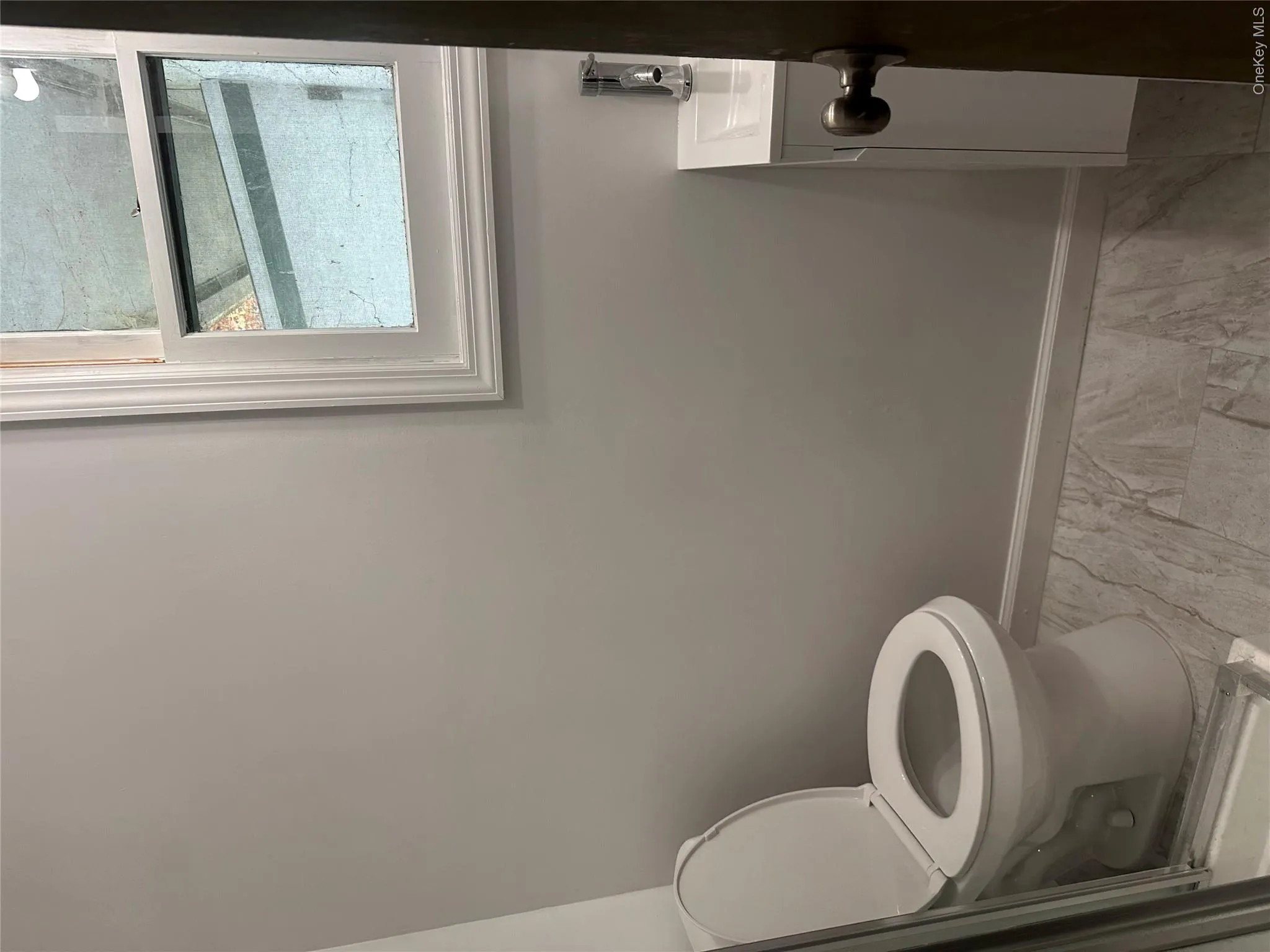 Bathroom featuring gray-toned wall paint, a white toilet, and gray stone-finish flooring Bathroom featuring gray-toned wall paint, a white toilet, and gray stone-finish flooring
