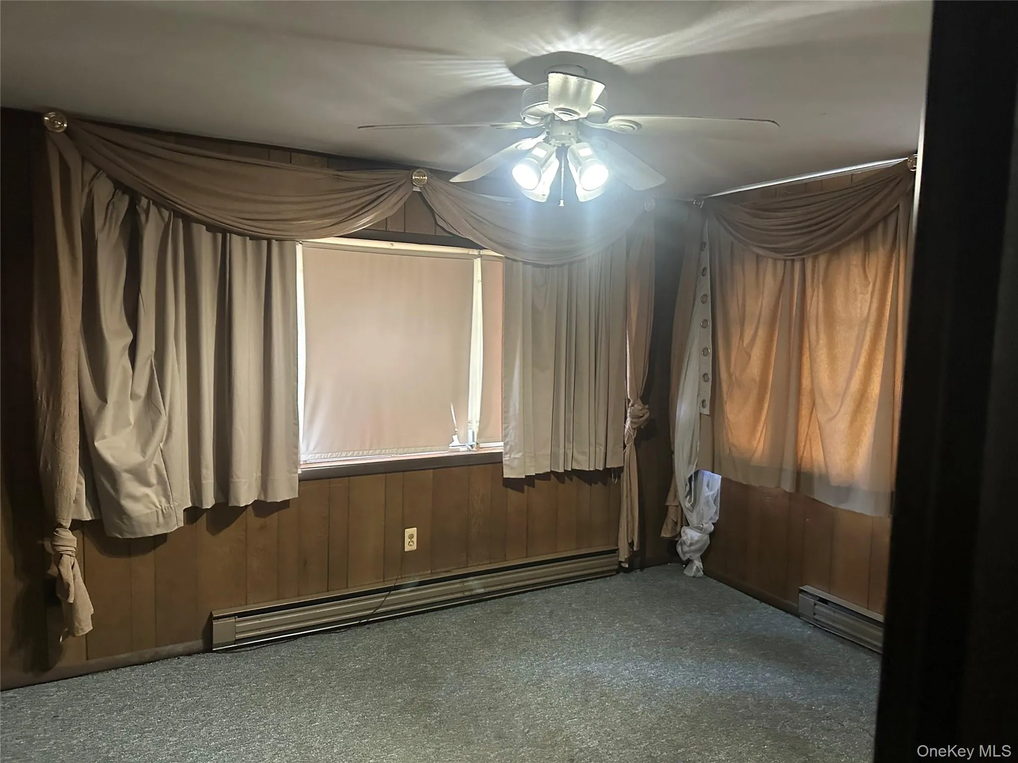 Carpeted room with wood paneling and a ceiling fan Carpeted room with wood paneling and a ceiling fan