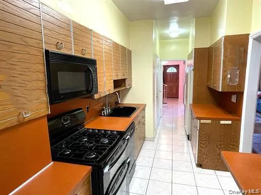 Galley kitchen featuring wood-finish cabinetry, solid surface countertops, and white tile flooring Galley kitchen featuring wood-finish cabinetry, solid surface countertops, and white tile flooring