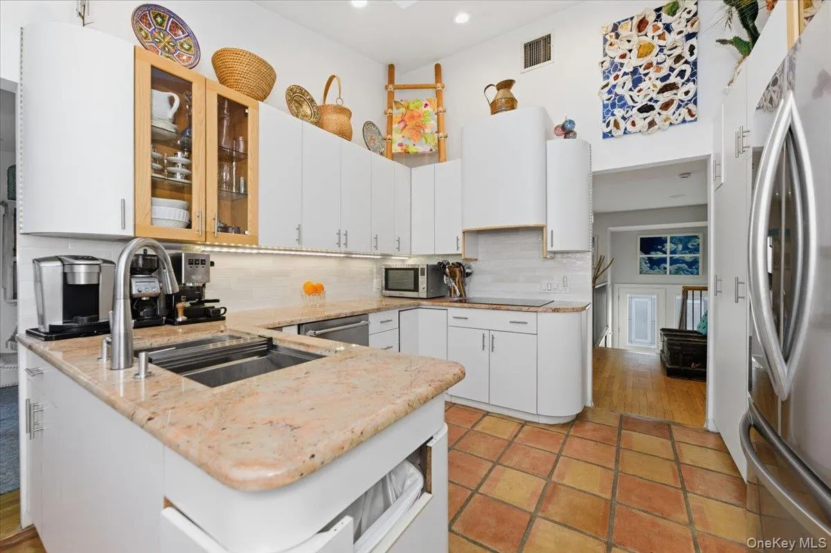 Kitchen featuring white cabinetry, stainless steel appliances, glass insert cabinets, backsplash, and light stone counters Kitchen featuring white cabinetry, stainless steel appliances, glass insert cabinets, backsplash, and light stone counters