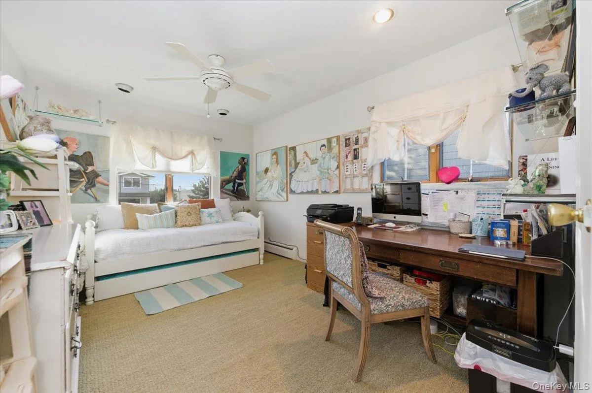 Bedroom featuring light colored carpet, a ceiling fan, a desk, and a baseboard radiator Bedroom featuring light colored carpet, a ceiling fan, a desk, and a baseboard radiator