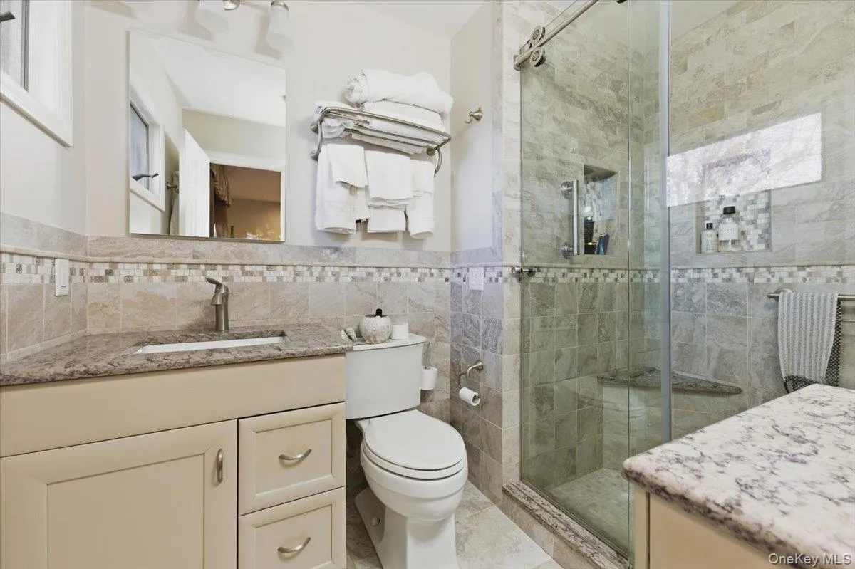 Full bath featuring vanity, tile walls, a shower stall, and wainscoting Full bath featuring vanity, tile walls, a shower stall, and wainscoting