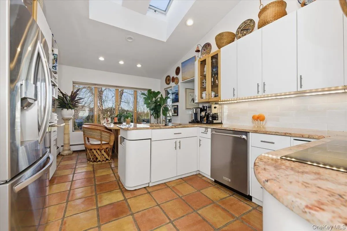 Kitchen featuring a skylight, vaulted ceiling, appliances with stainless steel finishes, glass insert cabinets, and white cabinets Kitchen featuring a skylight, vaulted ceiling, appliances with stainless steel finishes, glass insert cabinets, and white cabinets