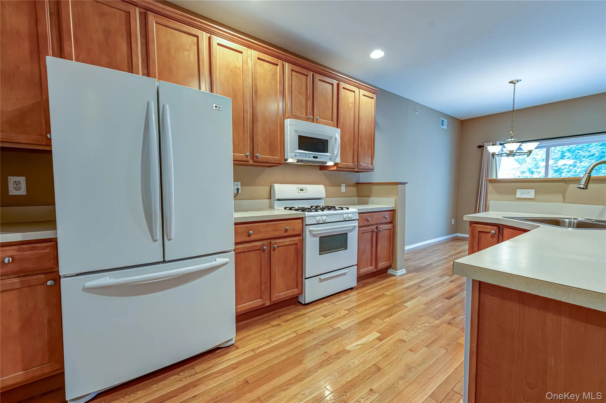 Kitchen featuring wood-finish cabinetry, light-toned countertops, a white gas range, and a white microwave Kitchen featuring wood-finish cabinetry, light-toned countertops, a white gas range, and a white microwave