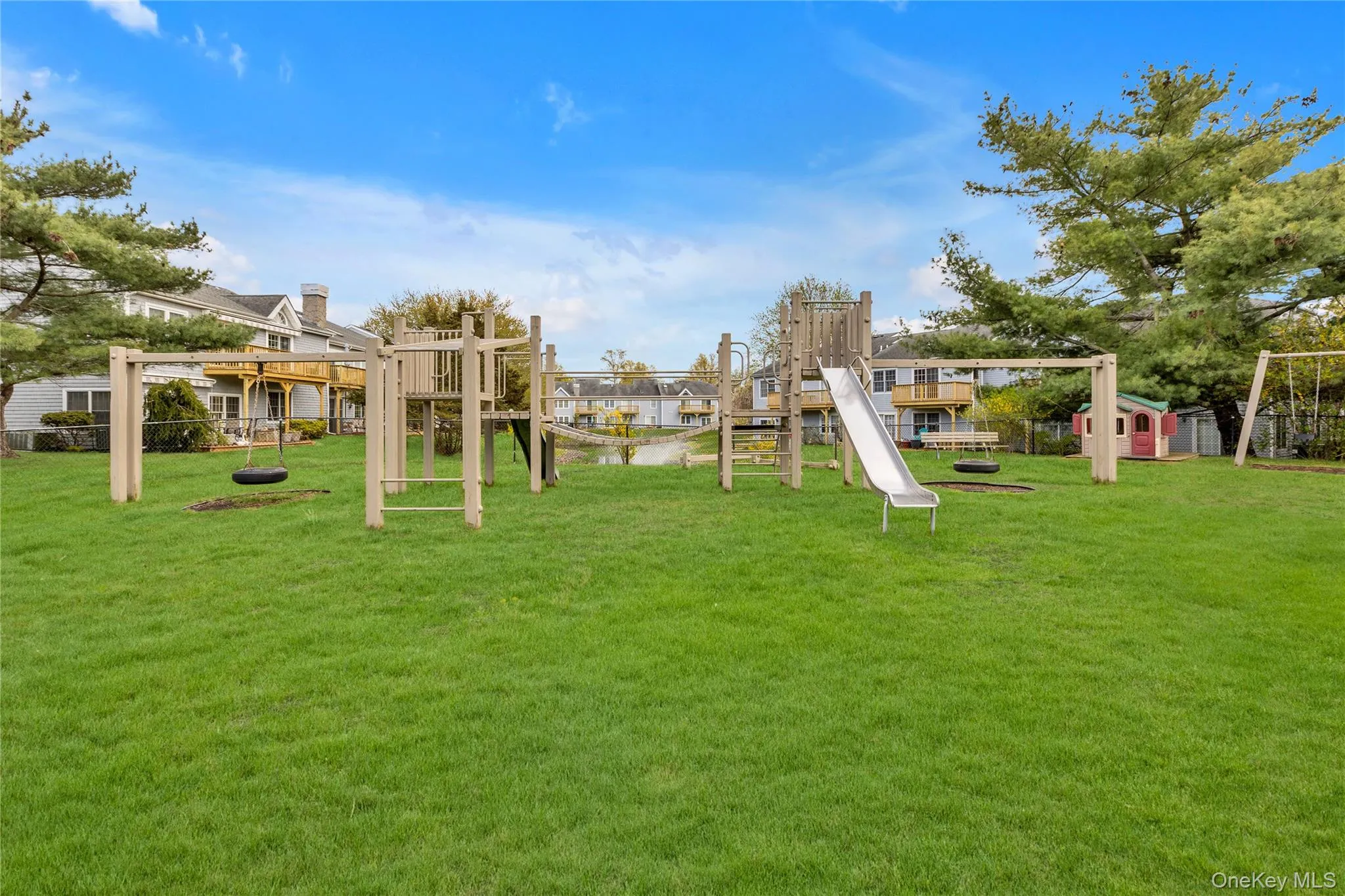 Expansive green space featuring a large playset with slides, swings, and climbing structures Expansive green space featuring a large playset with slides, swings, and climbing structures