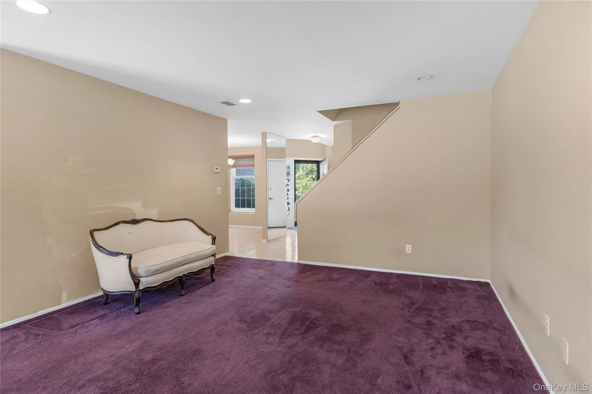 Spacious room with plush carpeting and neutral tone walls, featuring a staircase to second level Spacious room with plush carpeting and neutral tone walls, featuring a staircase to second level