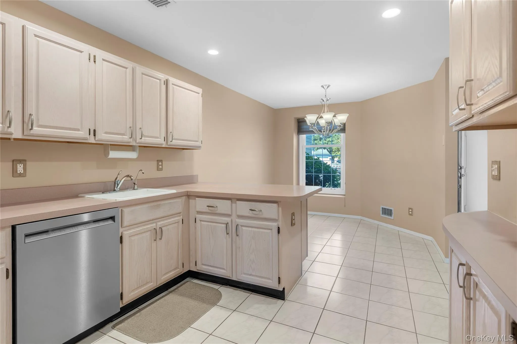 Kitchen featuring white cabinetry, light countertops, a stainless steel dishwasher, and white tile flooring Kitchen featuring white cabinetry, light countertops, a stainless steel dishwasher, and white tile flooring