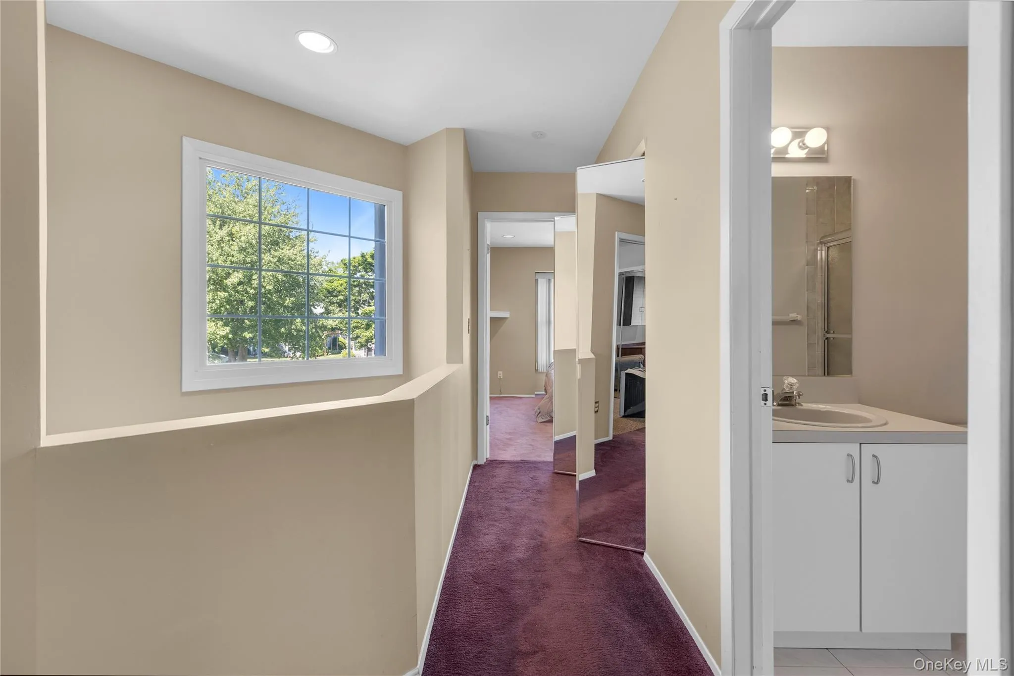 Hallway featuring a large window with grid pattern, neutral wall tones, recessed lighting, and burgundy carpeting Hallway featuring a large window with grid pattern, neutral wall tones, recessed lighting, and burgundy carpeting