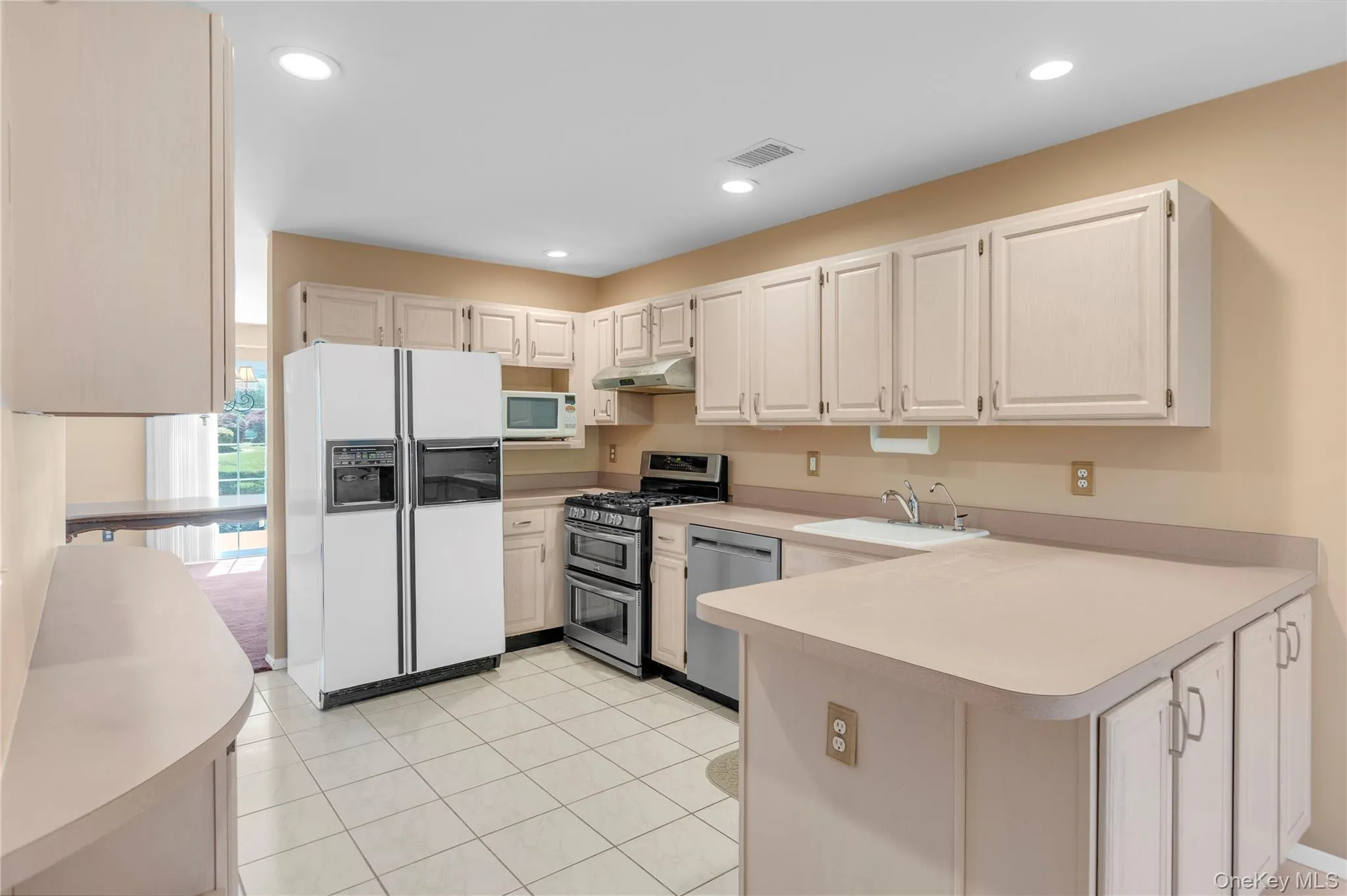 Kitchen featuring light-toned cabinetry, a double oven range, stainless steel dishwasher, and recessed lighting Kitchen featuring light-toned cabinetry, a double oven range, stainless steel dishwasher, and recessed lighting