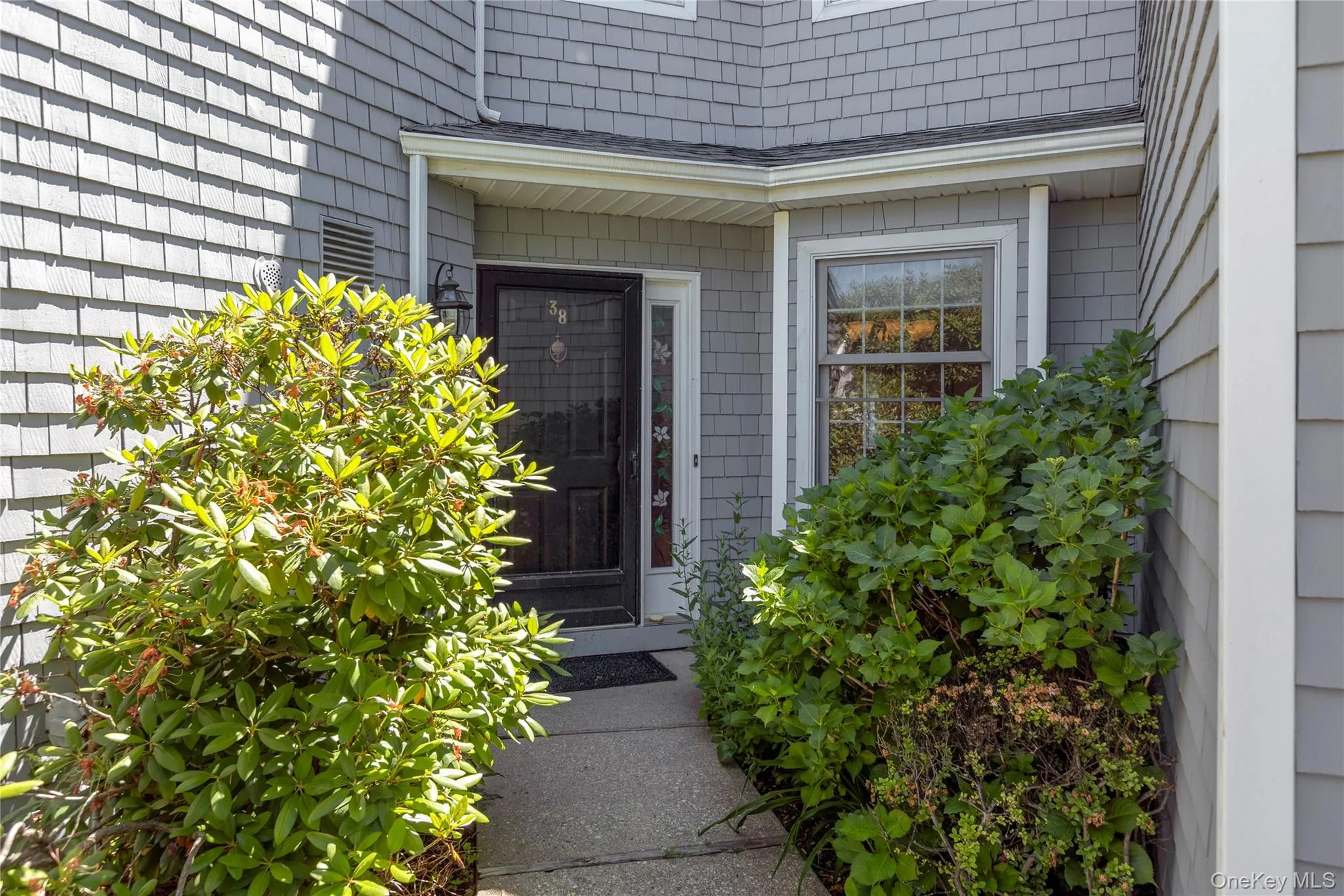 Entryway featuring a dark paneled door with a storm door, an overhead light fixture, and a single-pane window with white trim Entryway featuring a dark paneled door with a storm door, an overhead light fixture, and a single-pane window with white trim